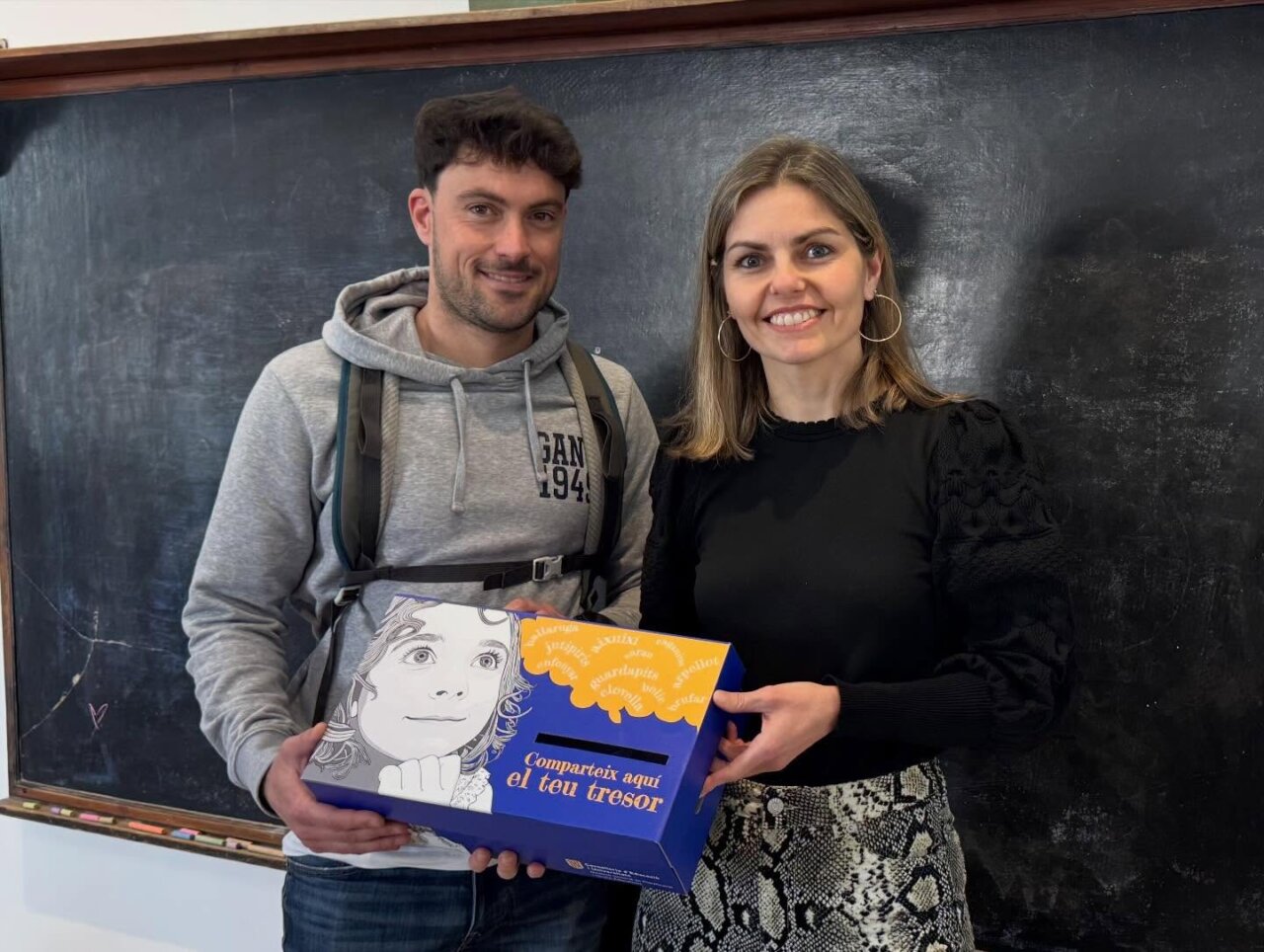 Dos personas sosteniendo una caja del proyecto educativo en un aula.