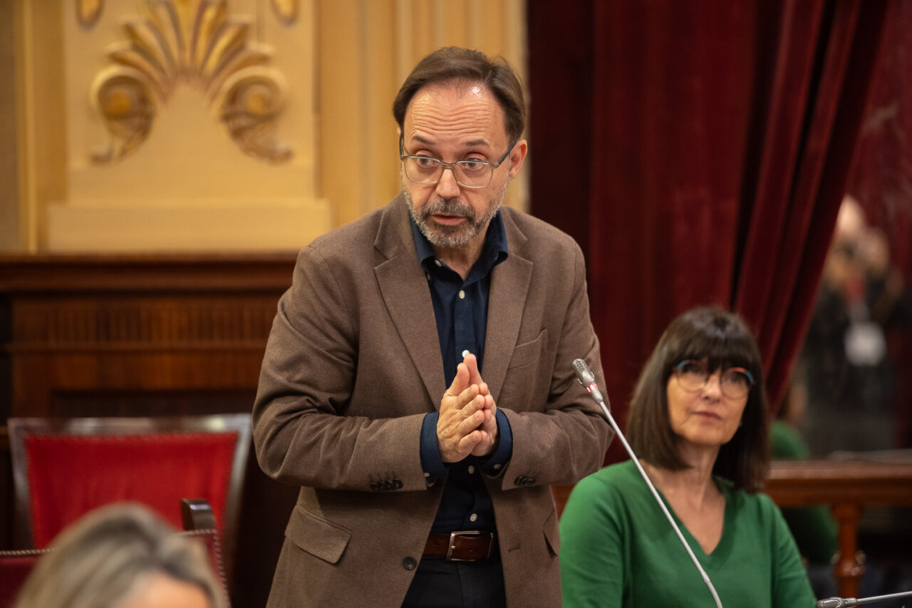 Un hombre hablando en el parlamento con una mujer detr&aacute;s.