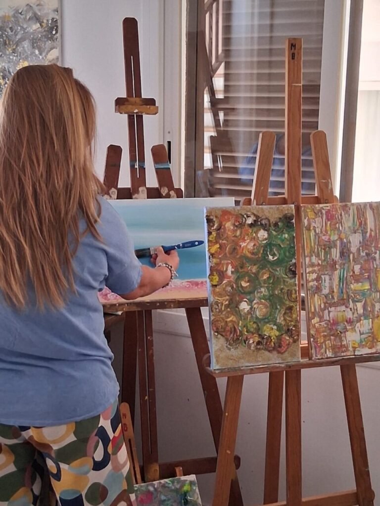 Mujer pintando en un caballete con obras de arte a su alrededor