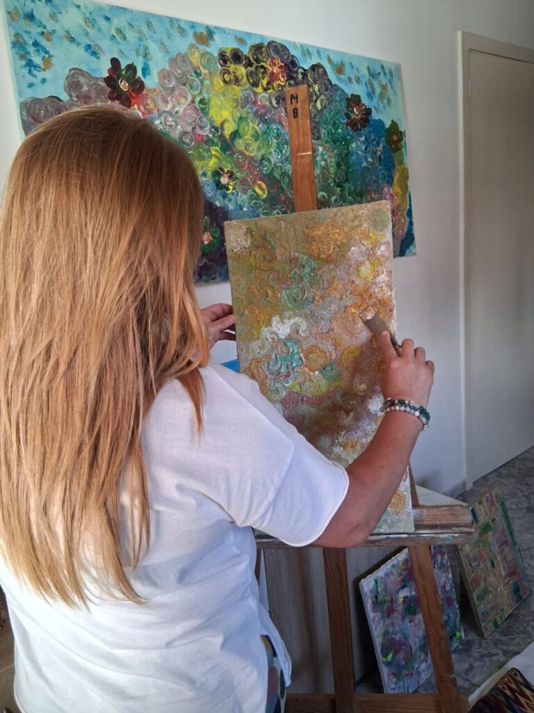 Virginia Siquier pintando en su estudio con obras coloridas detr&aacute;s.