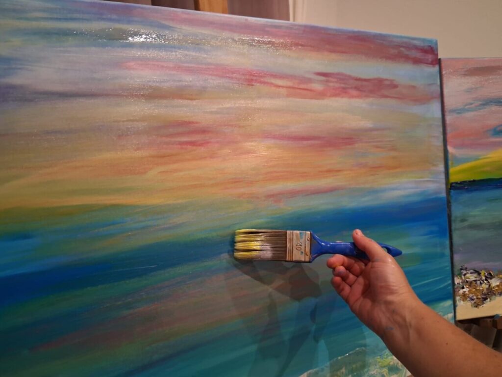Mano pintando un paisaje en un lienzo con brocha