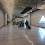 Pasillo de un aeropuerto con viajeros y pantallas de informaci&oacute;n