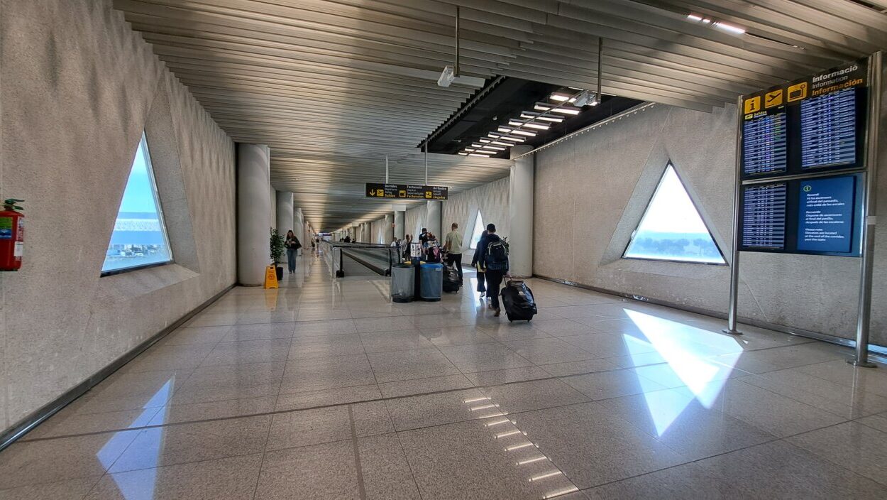 Pasillo de un aeropuerto con viajeros y pantallas de informaci&oacute;n
