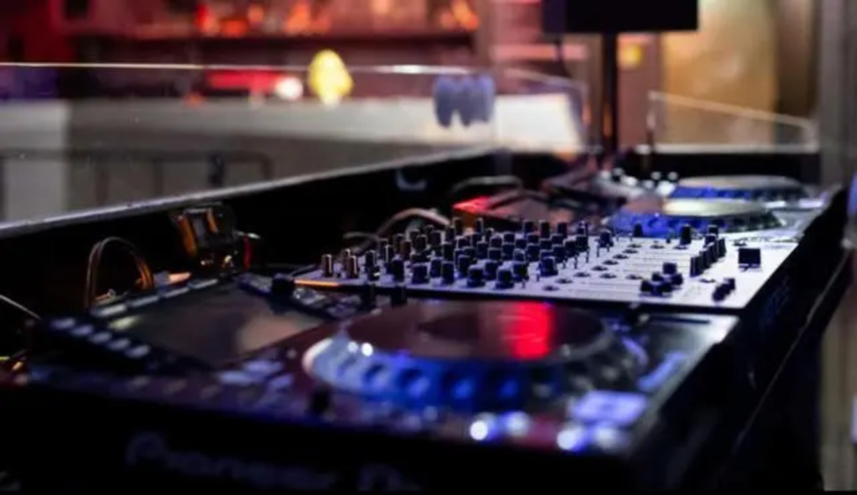 Cabina de DJ con equipo de mezcla y luces en un evento electr&oacute;nico