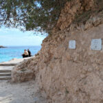 Vista de Cala Comtessa con placas informativas sobre rodajes históricos