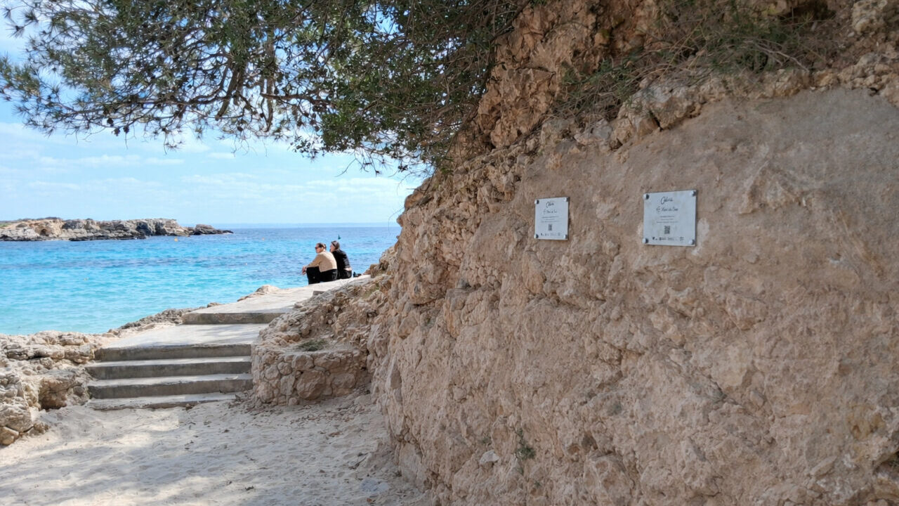Vista de Cala Comtessa con placas informativas sobre rodajes hist&oacute;ricos