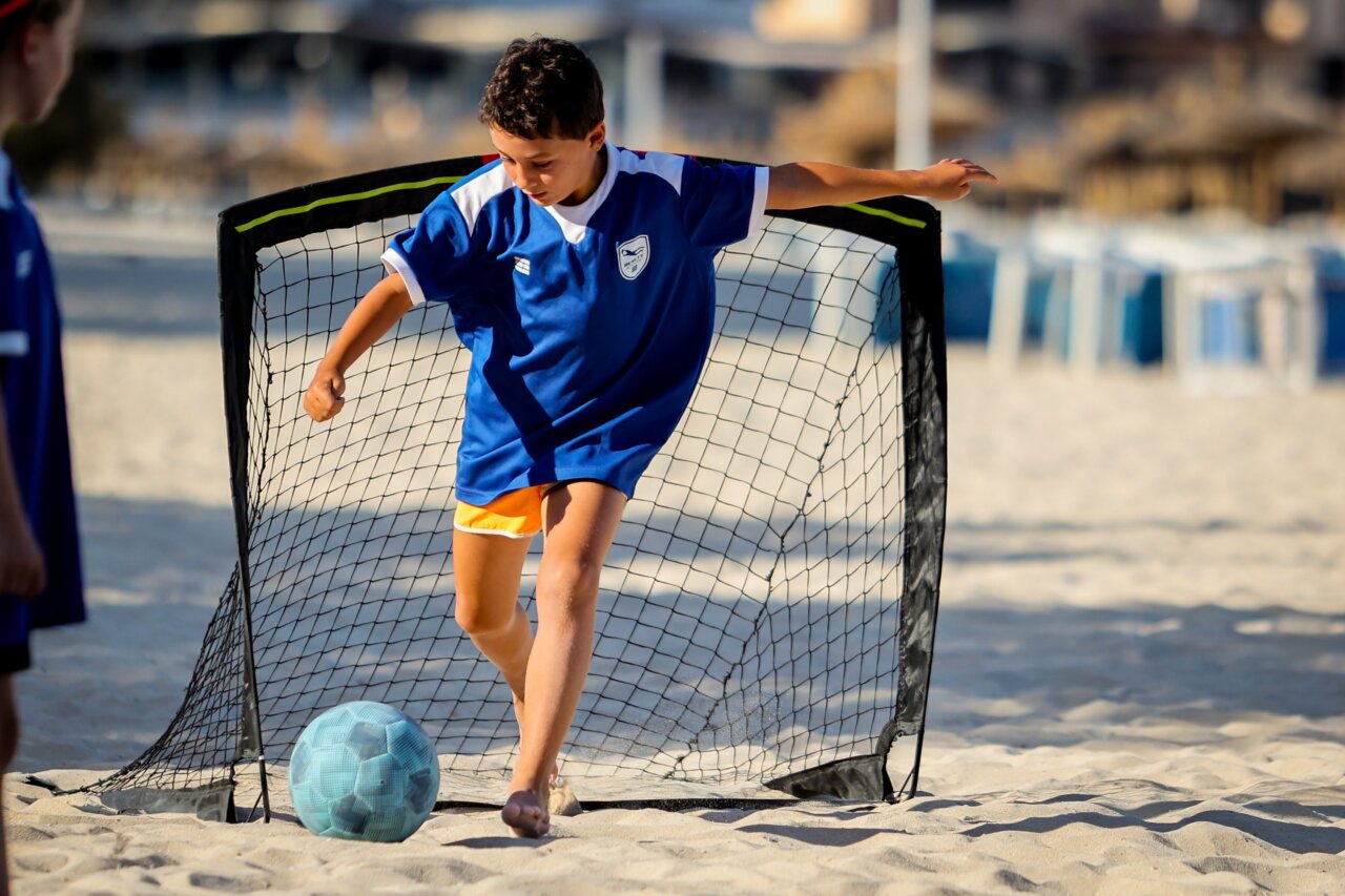 Niño jugando al fútbol en la playa durante un campamento de verano