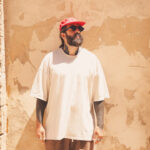 Deejay mallorqu&iacute;n con camiseta clara y gorra roja frente a una pared