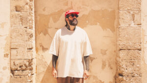 Deejay mallorqu&iacute;n con camiseta clara y gorra roja frente a una pared