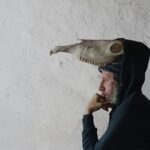 Hombre pensativo con un cr&aacute;neo en la cabeza en un fondo blanco