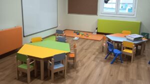 Aula de guarder&iacute;a con mesas y sillas coloridas para ni&ntilde;os peque&ntilde;os.