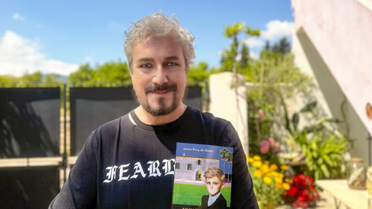 Jaime Roig de Diego sosteniendo su novela en un entorno ajardinado