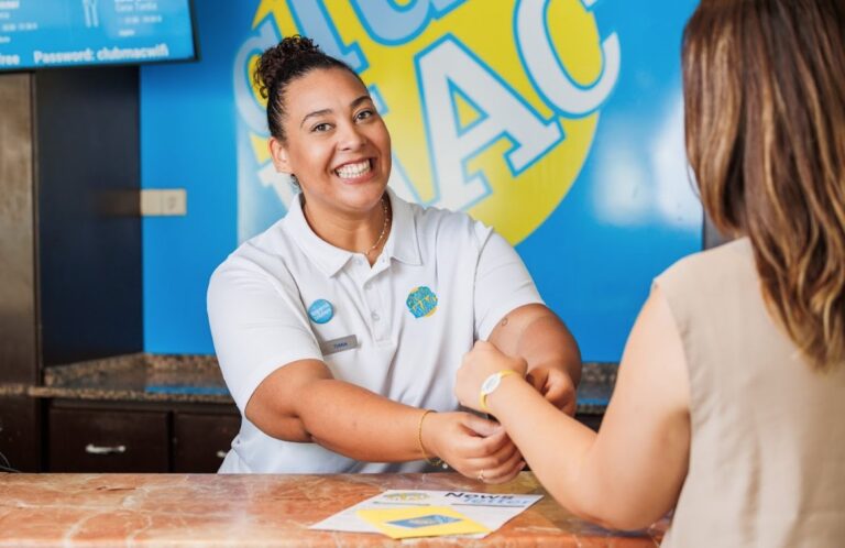 Recepcionista sonriente en Club Mac entregando una pulsera a un cliente
