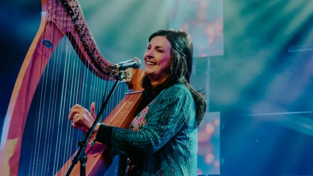 Moya Brennan tocando el arpa y cantando en un escenario iluminado