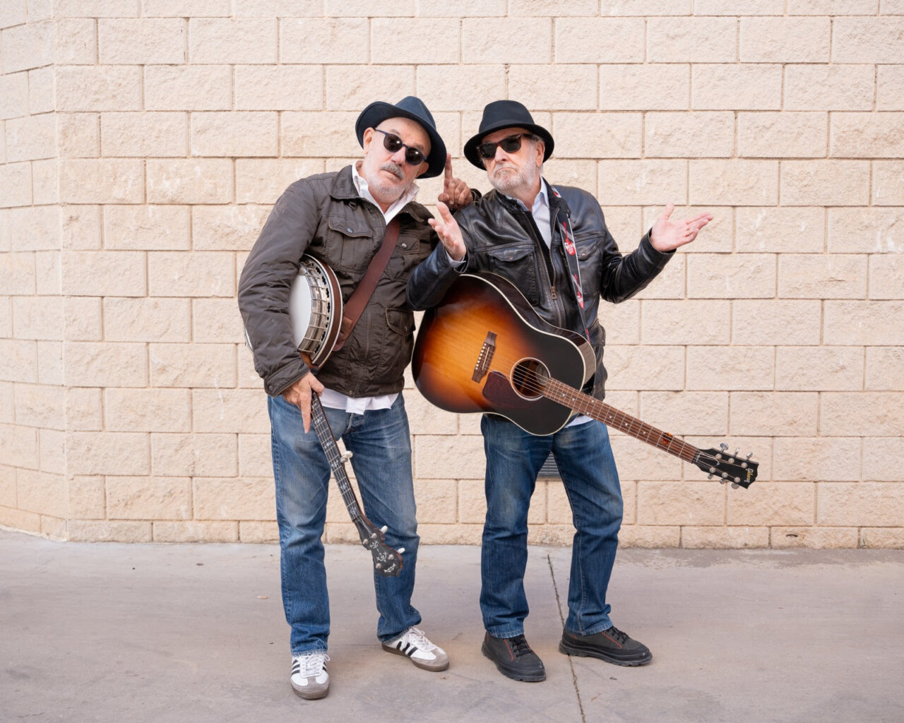 Dos m&uacute;sicos posando con instrumentos en un fondo de pared.
