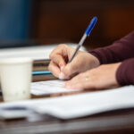 Mano escribiendo en un documento con bol&iacute;grafo en una mesa