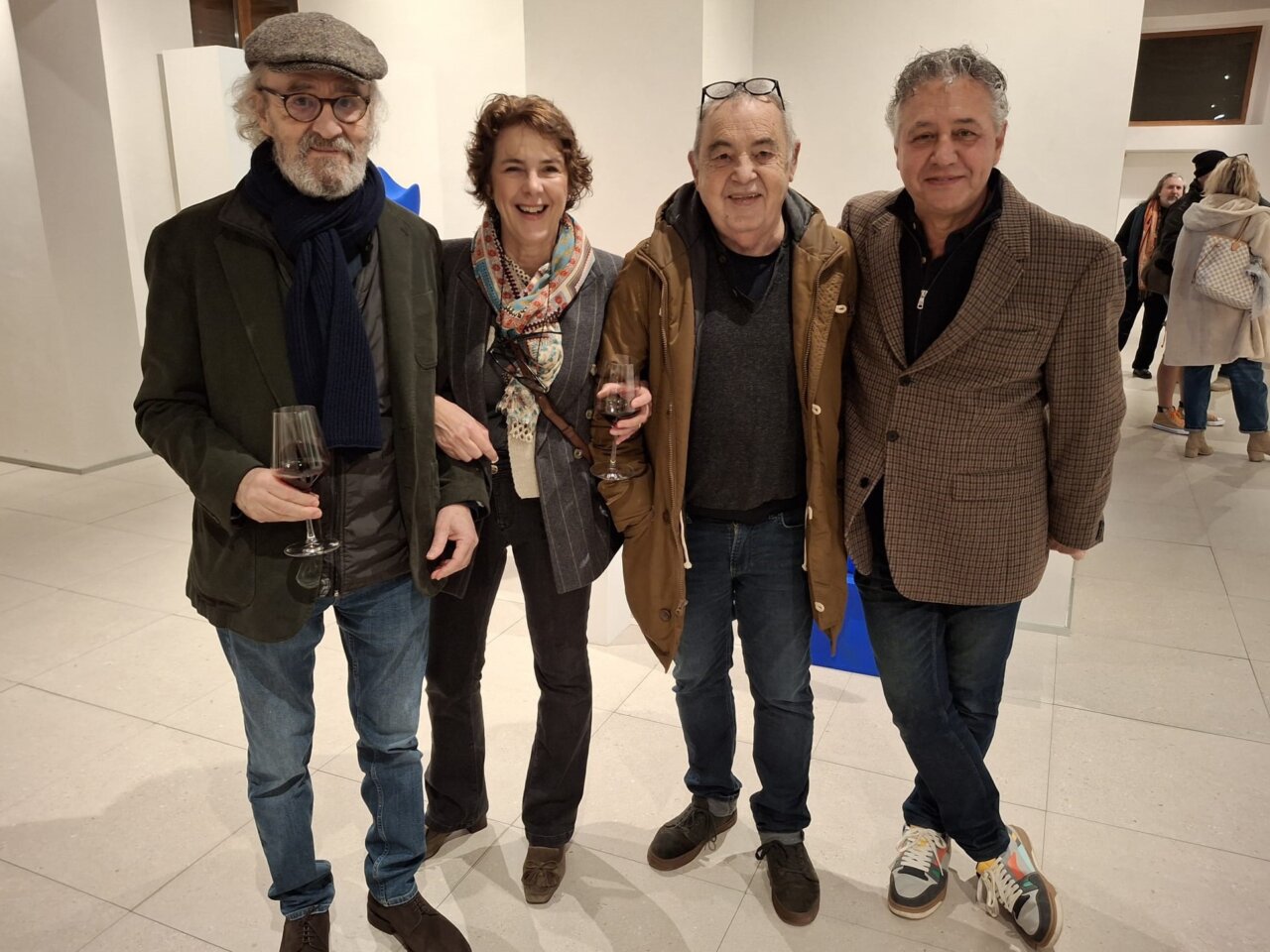 Cuatro personas en un evento artístico sosteniendo copas de vino.