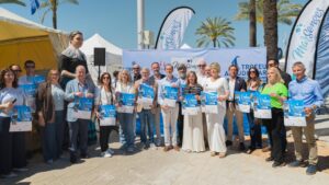 Presentaci&oacute;n de la regata solidaria en el puerto de Alc&uacute;dia con participantes y cartel