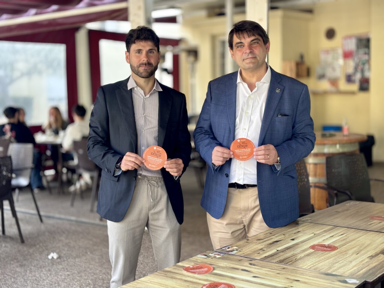 Dos hombres sosteniendo carteles en una terraza de cafetería de la UIB