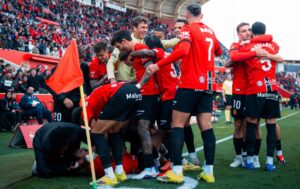 Jugadores del RCD Mallorca celebrando un gol en el estadio con aficionados al fondo.