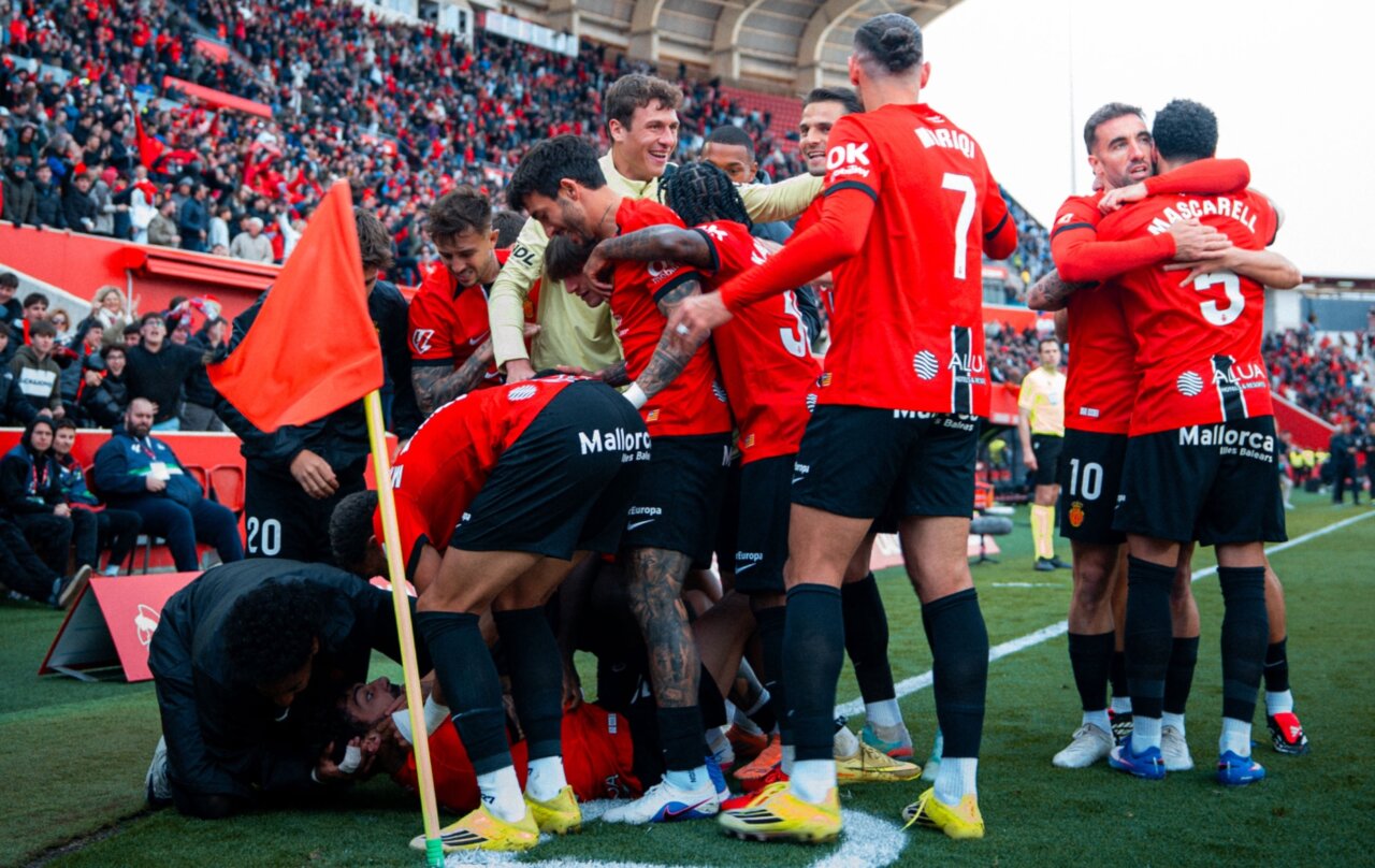 Jugadores del RCD Mallorca celebrando un gol en el estadio con aficionados al fondo.
