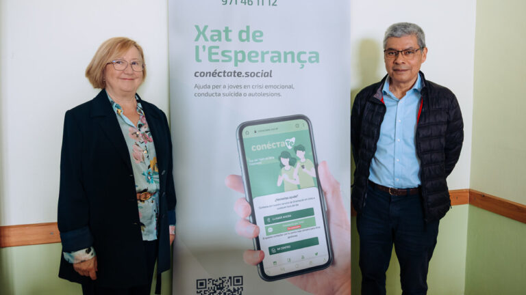 Dos personas junto a un cartel del Tel&eacute;fono de Esperanza en las Islas Baleares