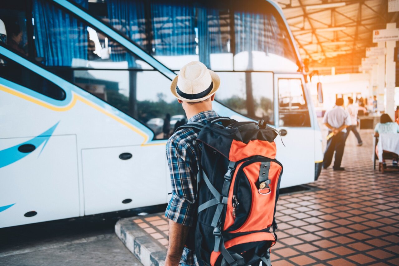 Turista con mochila esperando un autob&uacute;s en una estaci&oacute;n