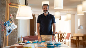 Hombre sonriente de pie frente a una mesa con documentos y materiales