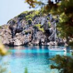 Barco de alquiler en aguas cristalinas de Ibiza rodeado de rocas