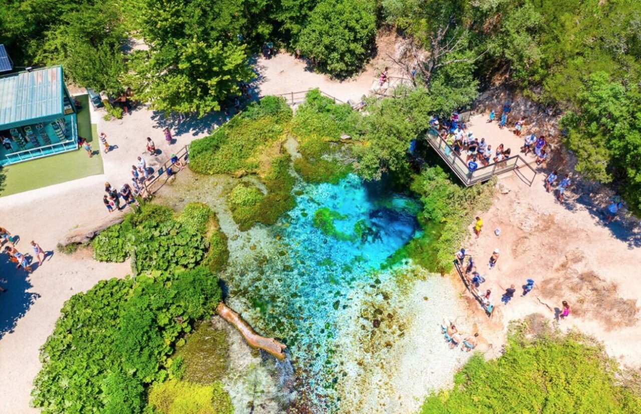 Vista a&eacute;rea de un lago azul rodeado de vegetaci&oacute;n y personas