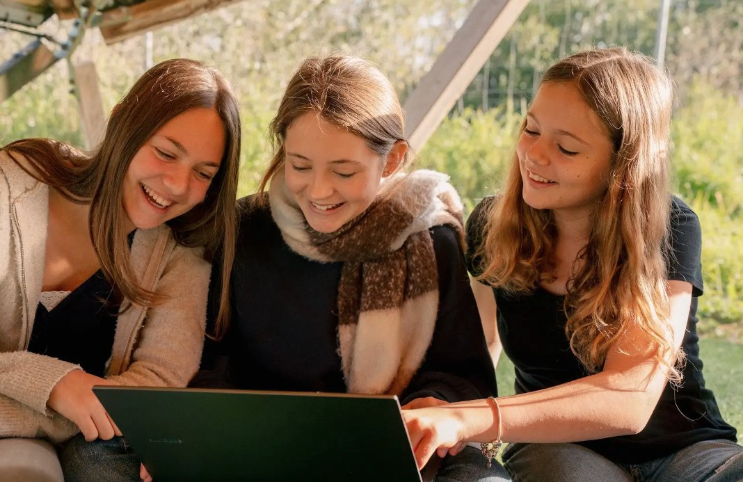 Tres adolescentes sonrientes interactuando con una computadora port&aacute;til al aire libre