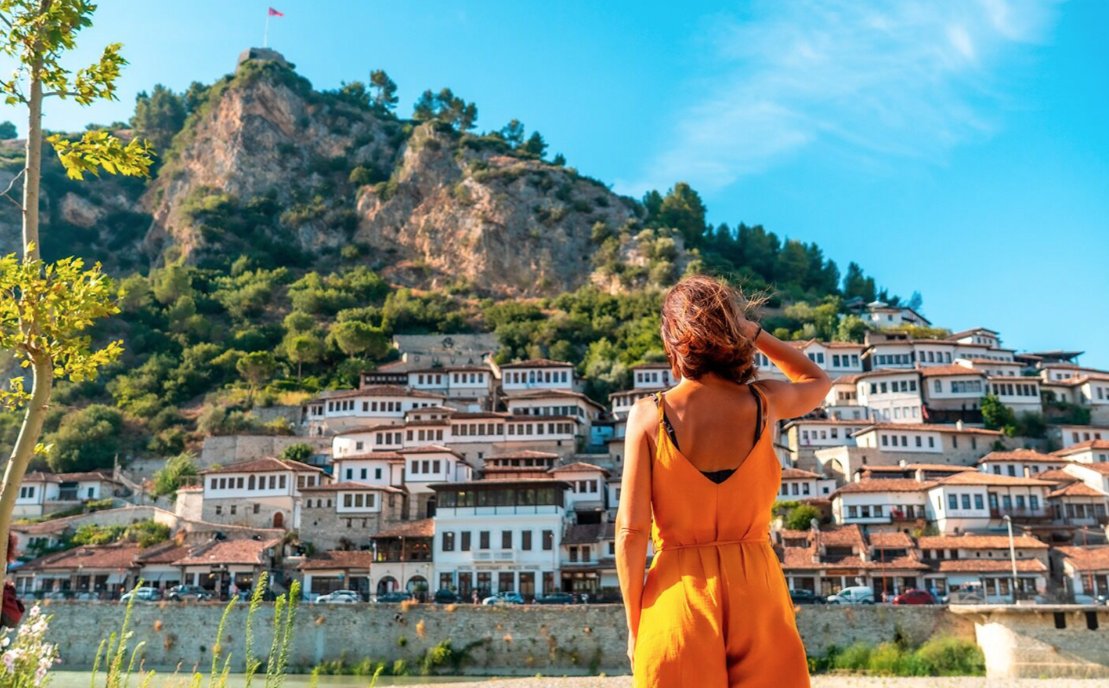 Mujer mirando casas tradicionales en Albania con monta&ntilde;as al fondo
