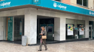 Exterior de la oficina de Cajamar con una mujer usando su tel&eacute;fono m&oacute;vil