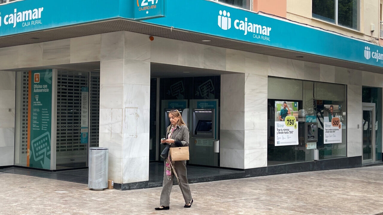 Exterior de la oficina de Cajamar con una mujer usando su tel&eacute;fono m&oacute;vil
