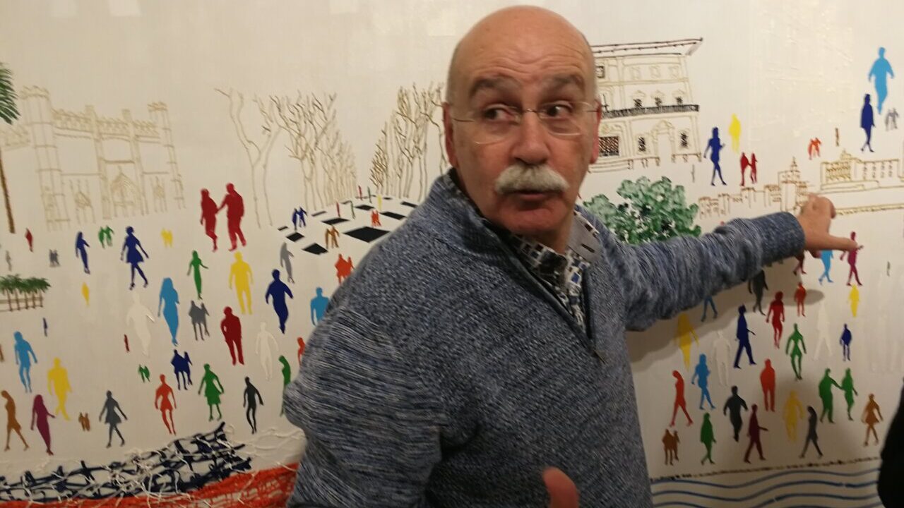Hombre explicando un mural colorido con figuras humanas.
