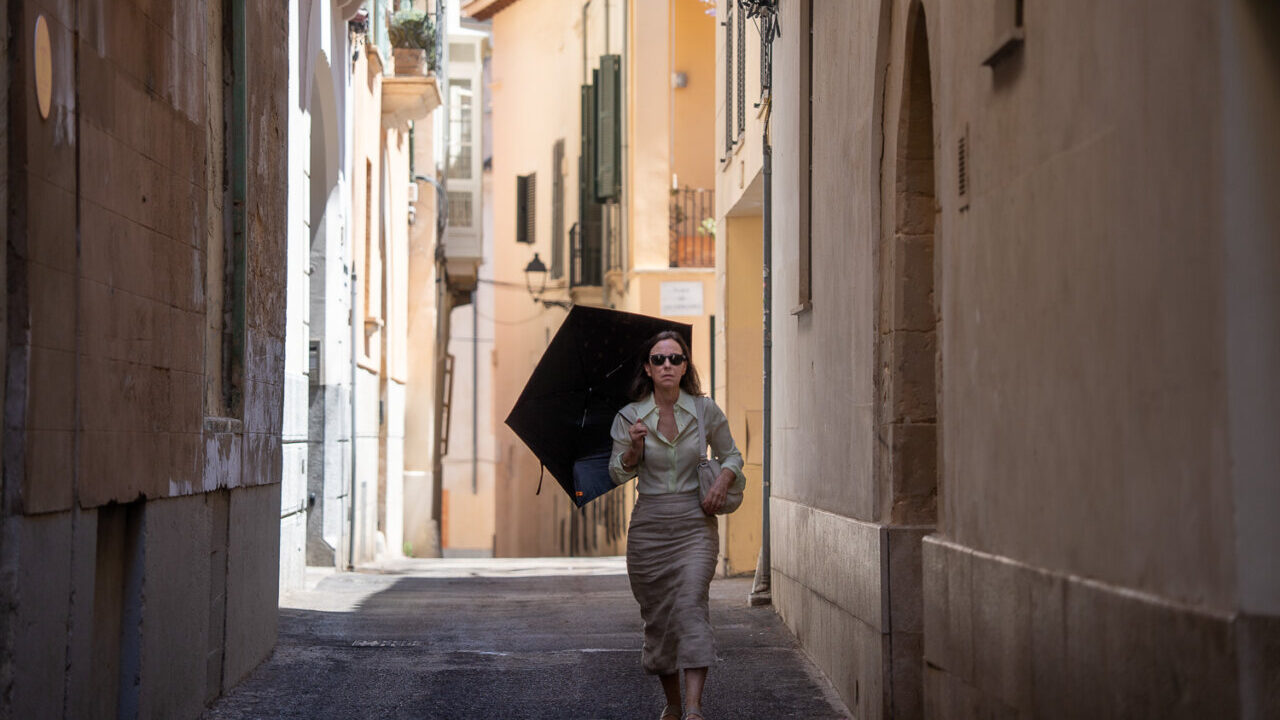 Mujer caminando por una calle estrecha con un paraguas en Mallorca