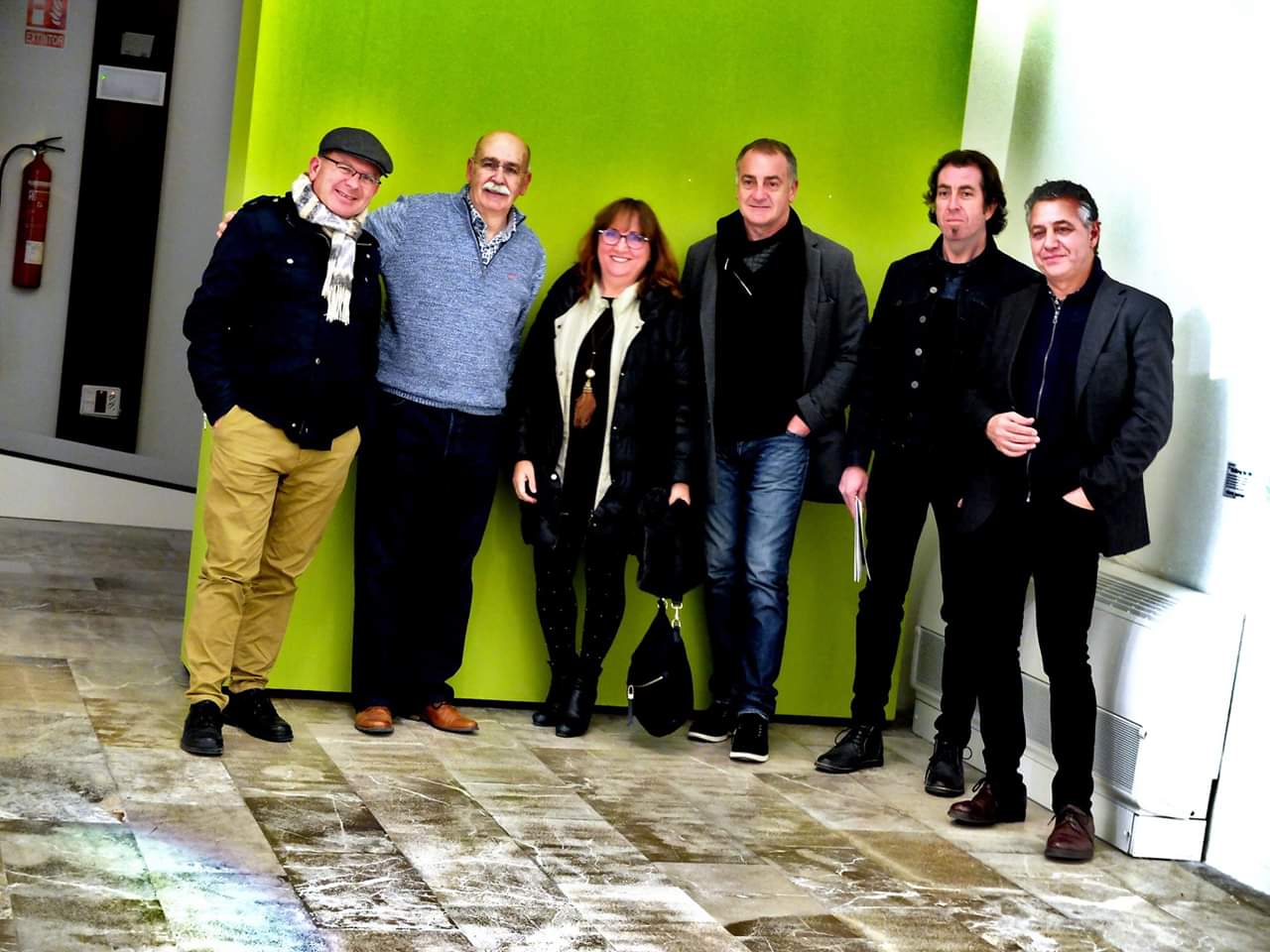 Grupo de seis personas posando frente a una pared verde
