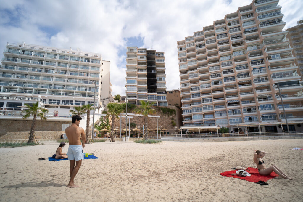 Vista de un edificio da&ntilde;ado por incendio en Magaluf con personas en la playa