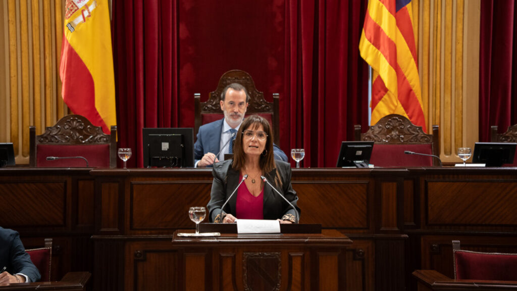 Mujer hablando en el Parlamento con banderas de España y Cataluña de fondo