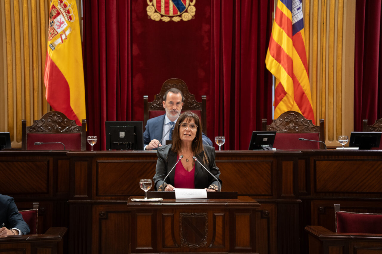 Mujer hablando en el Parlamento con banderas de España y Cataluña de fondo
