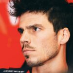 Joan Mir en el box de MotoGP, con expresi&oacute;n seria y fondo rojo.