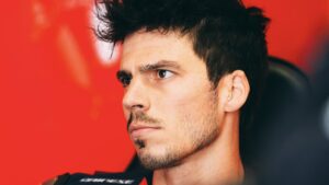 Joan Mir en el box de MotoGP, con expresi&oacute;n seria y fondo rojo.
