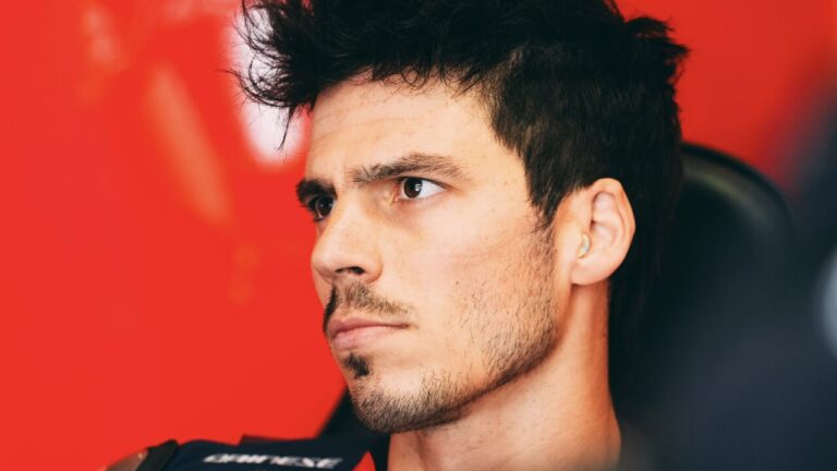 Joan Mir en el box de MotoGP, con expresi&oacute;n seria y fondo rojo.