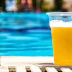 Vaso de cerveza amarilla al lado de una piscina azul