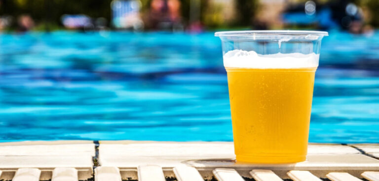 Vaso de cerveza amarilla al lado de una piscina azul