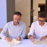 Dos hombres firmando documentos en un evento sobre viviendas en ParcBit