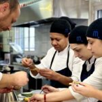 Chef y estudiantes en cocina preparando platos en formación profesional