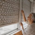 Mujer mayor ajustando una persiana en su hogar.