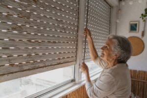 Mujer mayor ajustando una persiana en su hogar.