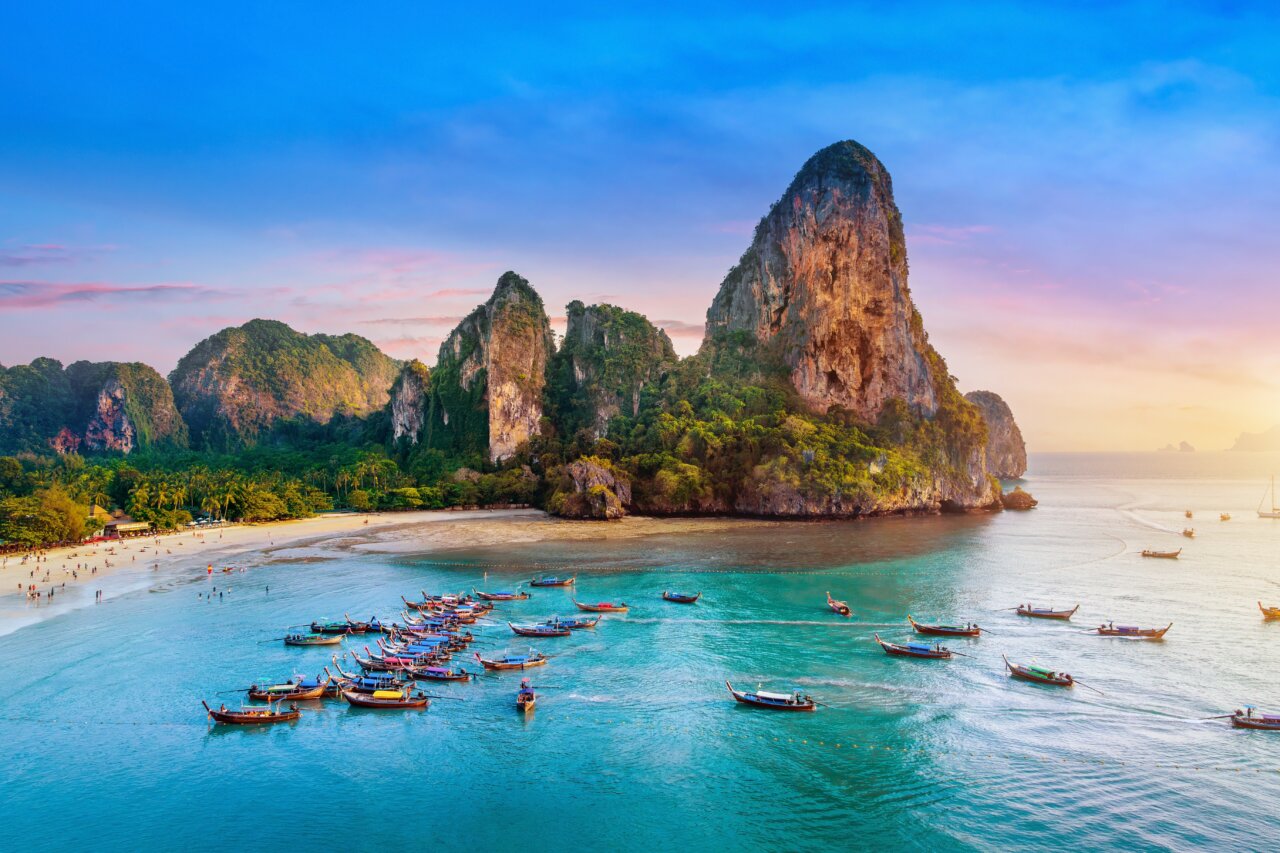 Vista de una playa en Tailandia con botes de madera y montañas al fondo